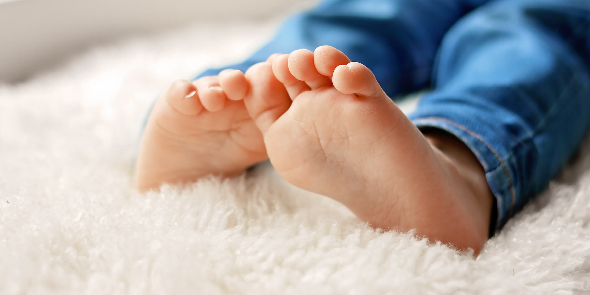 Clinique podiatrique Stéphanie Brodeur | Gros plan sur les pieds d'un enfant assis sur un tapis de mouton blanc